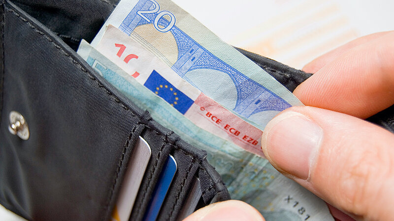 Eine Person holt Geldscheine aus einem Portemonnaie , Bild: Stockwerk-Fotodesign / adobe.stock.com
