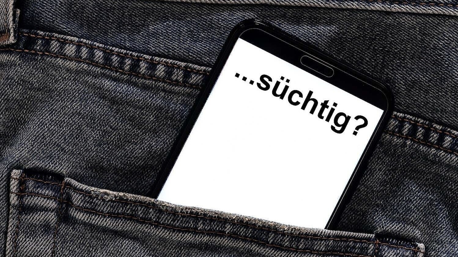 Aus einer Hosentasche ragt ein Handy auf dem "...süchtig?" steht. 