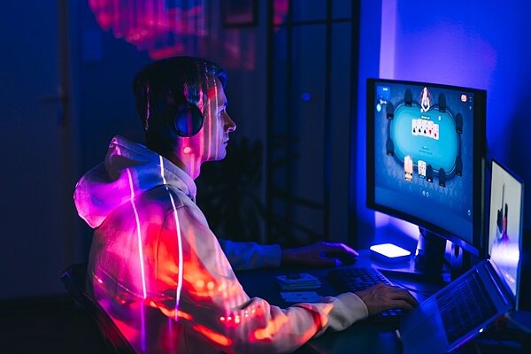 Junger Mann sitzt mit Kopfhörern vor dem Computer und spielt Online-Poker.