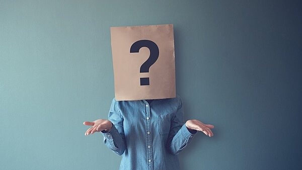 Eine Frau mit einer Papiertüte auf dem Kopf, auf der ein Fragezeichen abgebildet ist. Das Bild symbolisiert die Frage, was typische Persönlichkeitseigenschaften von Menschen mit problematischem Spielverhalten sind. 